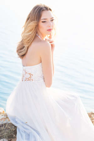Beautiful young woman outdoors portrait, vogue bride romantic girl on rocks at sea, gorgeous female summer, elegant lady at sea on nature, beauty brunette at sunset enjoying the sunの写真素材