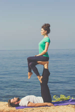 Couple practicing acroyoga in the morning, girl sitting on the mens feetsの写真素材