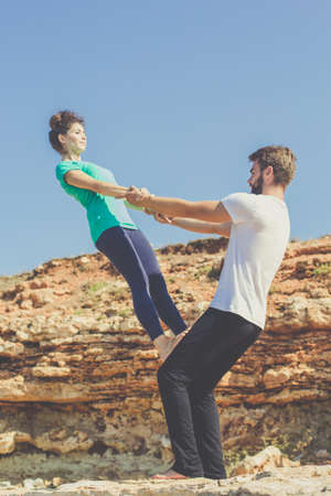 Young sportive couple man and woman  are practicing acroyoga exercises in the early morning on the beach with stonesの写真素材