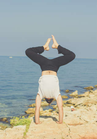 Young sportive man is practicing acroyoga exercises in the early morning on the beach with stonesの写真素材