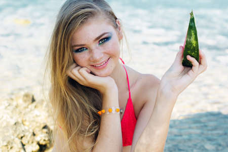 Beauty smiling teenager girl is wearing pink bikini and eating watermelon near seaの写真素材