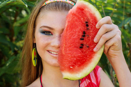 Beautiful face of happy teenager girl with fashion makeup is eating watermelon outdoorsの写真素材