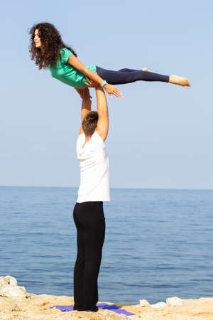 Young sportive couple are practicing acroyoga exercises in the early morning on the sea coastの写真素材