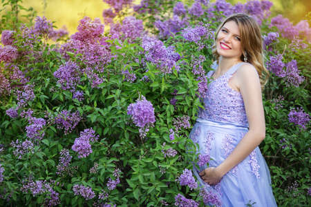 Happy pregnant girl is wearing fashion purple dress with big belly sitting in spring blossom garden with lilac flowersの写真素材