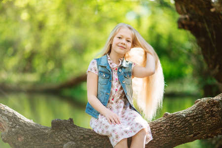 Cute little girl sitting on log under riverの写真素材