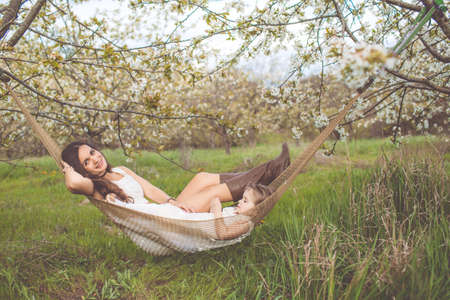 Happy girl with mother is resting in hammock outdoorsの写真素材