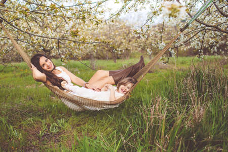 Happy girl with mother is resting in hammock outdoorsの写真素材
