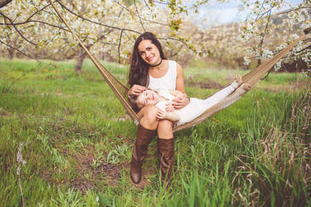 Happy mother and daughter are resting in hammock outdoorsの写真素材