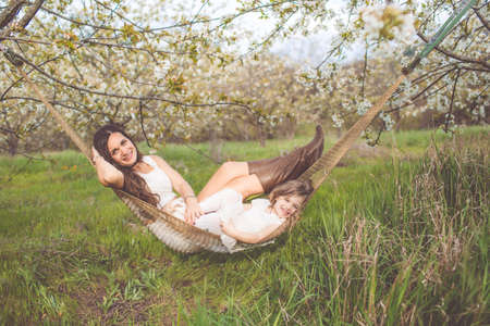 Happy mother and daughter are resting in hammock outdoorsの写真素材