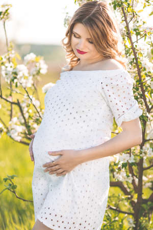 Happy pregnant woman in white blossom gardenの写真素材
