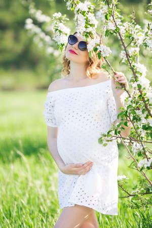 Happy pregnant young woman in white blossom gardenの写真素材