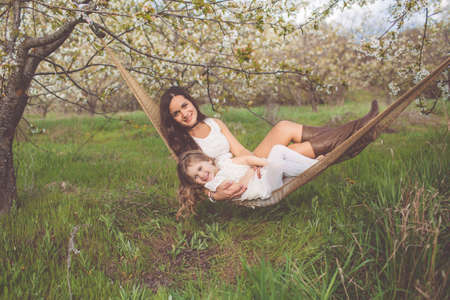 Happy mother and child girl are resting in hammock outdoorsの写真素材
