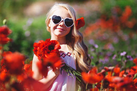 Child girl is wearing sunglasses in spring field with poppiesの写真素材