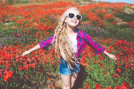 Child girl is wearing sunglasses and casual clothes in spring field with bouquet of poppiesの写真素材