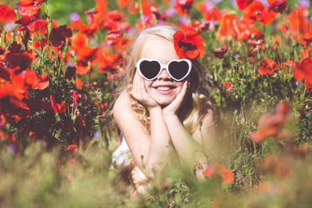 Child girl is wearing sunglasses in spring field with poppiesの写真素材