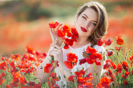 Pretty woman in field of red poppy flowers, spring timeの写真素材