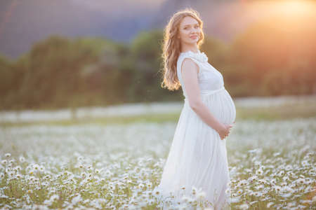 Beautiful happy pregnant girl on the field of daisy flowersの写真素材