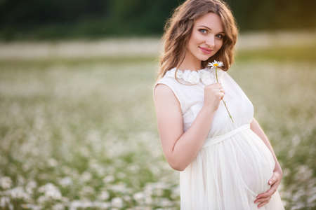 Beautiful pregnant woman on the field of daisy flowersの写真素材