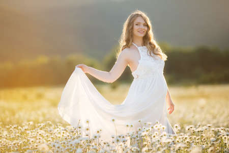 Beautiful happy pregnant girl on the field of daisy flowers, sunset timeの写真素材