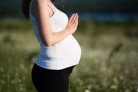 Beautiful pregnant woman doing yoga in the camomile field
