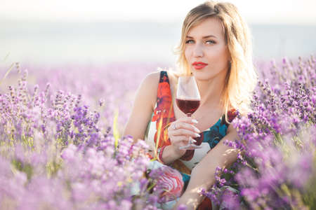 Beautiful blonde sexy woman is drinking red dry wine in lavender fieldの写真素材