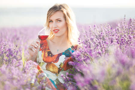 Beautiful blonde sexy woman is drinking red dry wine in lavender fieldの写真素材