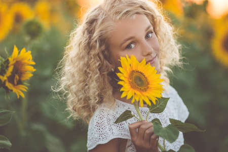 Happy pretty blonde girl in white dress having fun in field of yellow sunflowersの写真素材