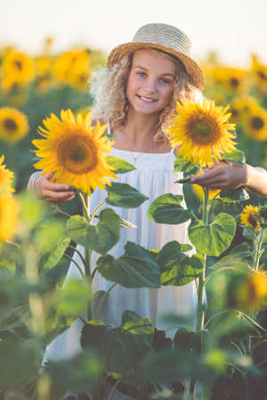 Curly pretty girl in white dress having fun in field of yellow sunflowersの写真素材