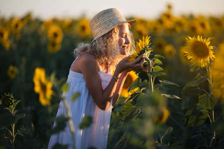 Happy pretty girl in white dress having fun in field of yellow sunflowersの写真素材