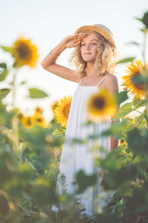 Curly pretty girl in white dress having fun in field of yellow sunflowersの写真素材