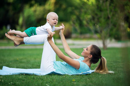 Sportive pretty mother is doing workout on lawn with little son. Sports concept, summer timeの写真素材