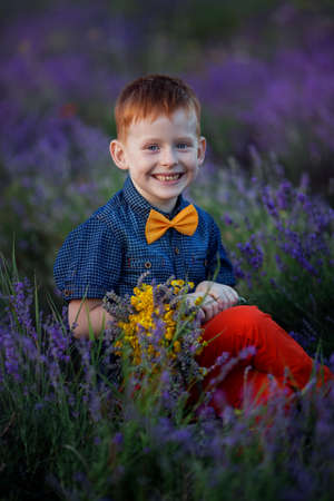 Happy fashion boy in lavender summer field with lavender bouquet in hands at sunset.の写真素材