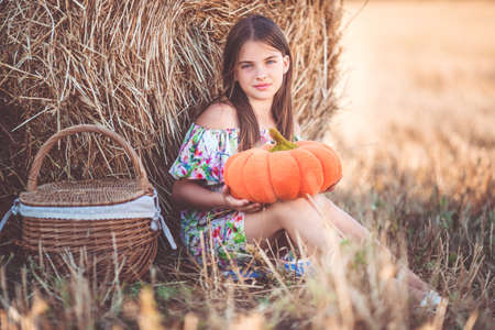 Pretty teenager girl near on stack of hay with basket and pumpkin in the fieldの写真素材