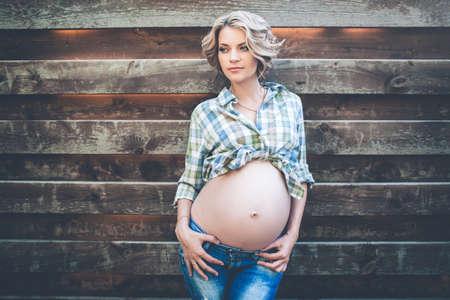 Beautiful pregnant girl is wearing casual clothes over wooden wallの写真素材