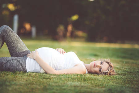 Beautiful slim sportive pregnant girl is lying on green lawnの写真素材