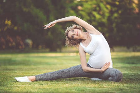 Beautiful slim sportive pregnant girl is doing sports on green grassの写真素材
