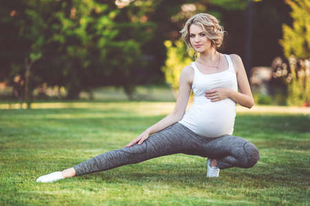 Beautiful slim sportive pregnant woman is doing sports on green grassの写真素材