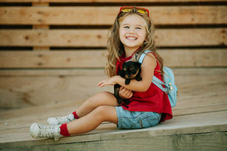 Happy smiling child girl is wearing fashion clothes with puppies of yorkshire terrier outdoorsの写真素材