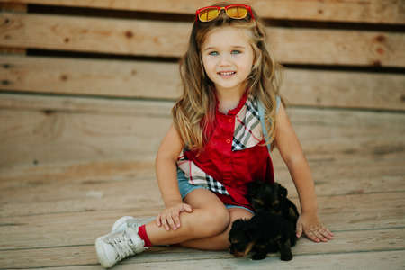 Happy smiling child girl is wearing fashion clothes with cute puppies of yorkshire terrier outdoorsの写真素材