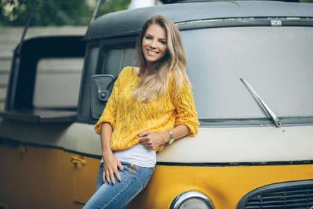 Fashion smiling woman is wearing yellow sweater near old retro busの写真素材