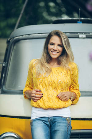 Happy smiling girl is wearing yellow sweater near old retro busの写真素材