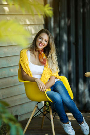 Fashion smiling woman is wearing yellow sweater sitting in yellow chair, autumn conceptの写真素材