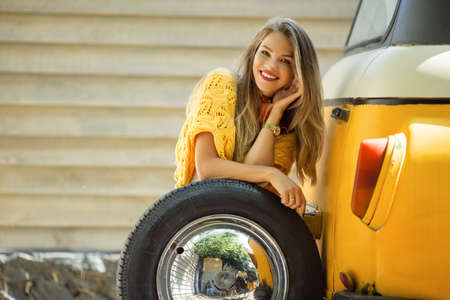 Happy smiling girl is wearing yellow sweater is posing with auto wheel near old retro bus, autumn conceptの写真素材