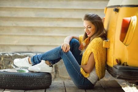 Happy smiling girl is wearing yellow sweater near old retro bus with tire, autumn conceptの写真素材