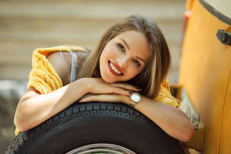 Happy smiling girl is wearing yellow sweater is posing with auto wheel near old retro bus, autumn conceptの写真素材