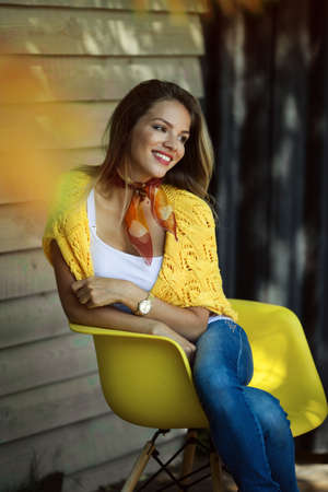 Fashion smiling woman is wearing yellow sweater sitting in yellow chairの写真素材