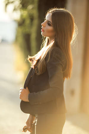Portrait of pretty serious business woman is wearing black official clothes near wooden wall over sunset lightsの写真素材