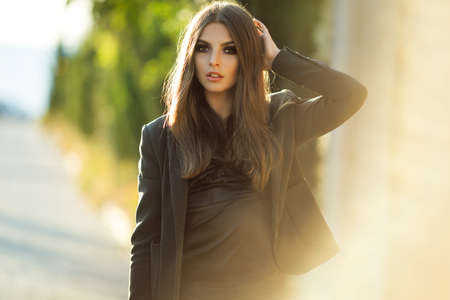 Portrait of pretty serious business woman is wearing black official clothes near wooden wall over sunset lightsの写真素材
