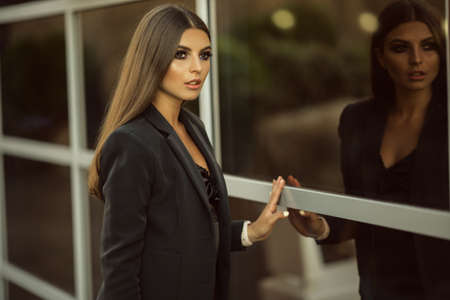 Portrait of fashion business girl is wearing black official clothes near big glass windows with reflectionの写真素材