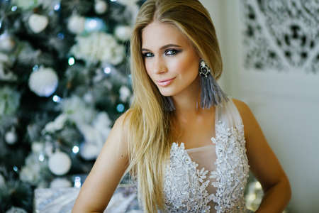 Beautiful blonde woman is sitting near decorated christmas tree with silver gift boxの写真素材
